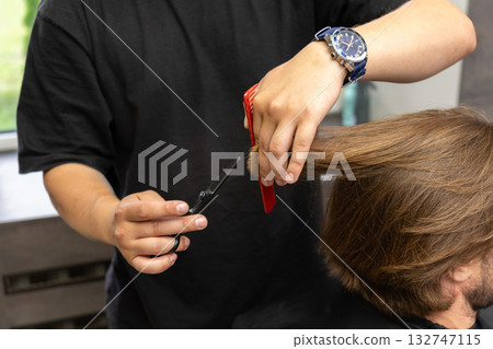 A hairdresser uses scissors and a comb to give a haircut to a client with long brown hair. 132747115