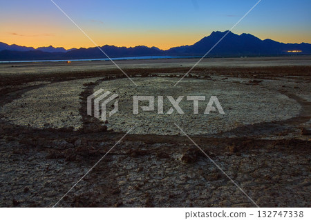 Cracked Dry Lake Bed With Tire Tracks And Mountains At Golden Hour 132747338