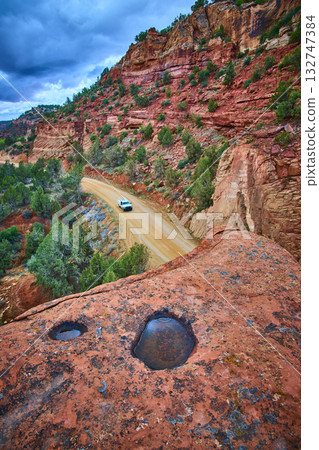 Winding Dirt Road Through Red Rock Canyon with White SUV and Rain Pools Utah 132747384