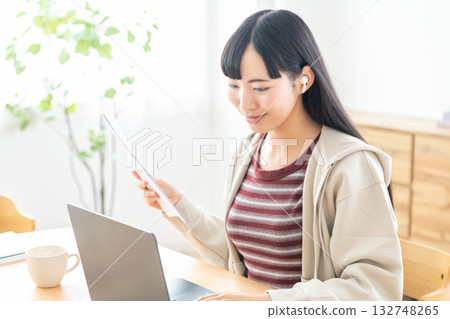 一位年輕女子手裡拿著一份文件，正在參加遠距會議。 132748265