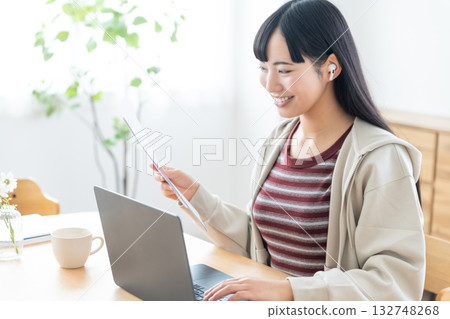 一位年輕女子手裡拿著一份文件，正在參加遠距會議。 132748268