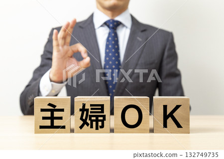 一名商人擺出「OK」的手勢，旁邊立著一塊寫著「家庭主婦OK」的積木。 132749735