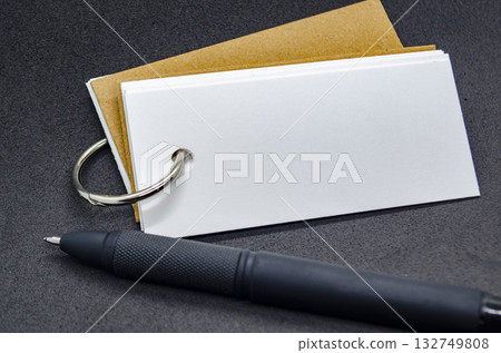 Close up of white banner shape notepad with customizable space for text on black cover background and with black pen. Close up of white banner shape notepad with customizable space for text on black cover background and with black pen. 132749808