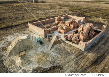 Aerial view of building site. Trenches dug in ground and filled with cement as foundation for future house, brick basement floor and stacks of brick for construction. 132749973