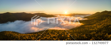 Aerial view of bright foggy morning over dark mountain forest trees at autumn sunrise. Beautiful scenery of wild woodland at dawn Aerial view of bright foggy morning over dark mountain forest trees at autumn sunrise. Beautiful scenery of wild woodland at dawn 132749977