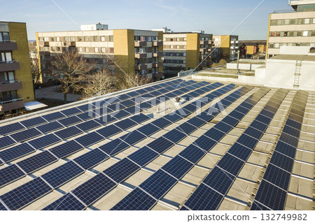Aerial view of blue shiny solar photo voltaic panels system on commercial roof producing renewable clean energy on city landscape background. 132749982
