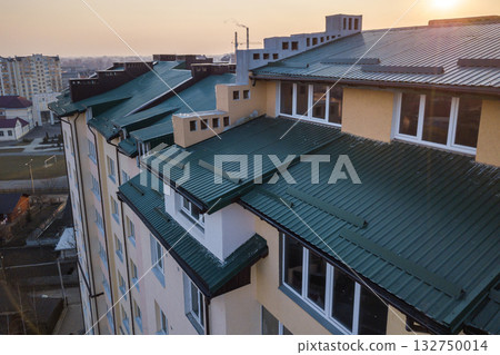 Aerial view of attic annex room exterior with plastic windows, roof and walls covered with green metal siding planks, new gutter system on top of high multi-storey apartment building. Aerial view of attic annex room exterior with plastic windows, roof and walls covered with green metal siding planks, new gutter system on top of high multi-storey apartment building. 132750014