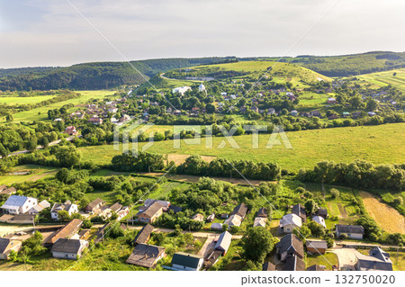 Aerial view of a small village win many houses and green agricultural fields in spring with fresh vegetation after seeding season on a warm sunny day. Aerial view of a small village win many houses and green agricultural fields in spring with fresh vegetation after seeding season on a warm sunny day. 132750020