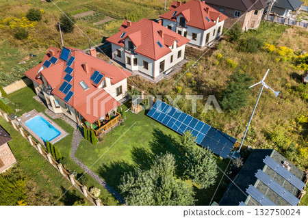 Aerial view of a new autonomous house with solar panels, water heating radiators on the roof, wind powered turbine and green yard with blue swimming pool. 132750024
