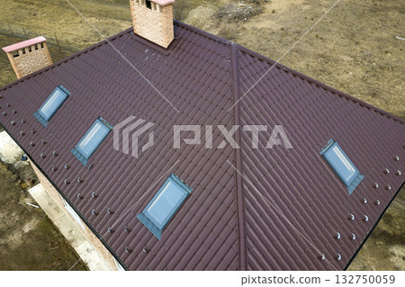 Aerial top view of building steep brown shingle roof, brick chimneys and small attic windows on house top with metal tile roof. Roofing, repair and renovation work. Aerial top view of building steep brown shingle roof, brick chimneys and small attic windows on house top with metal tile roof. Roofing, repair and renovation work. 132750059