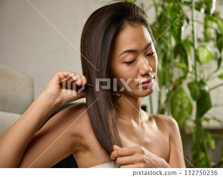Young woman brushing long hair with peaceful focus in morning light Young woman brushing long hair with peaceful focus in morning light 132750236