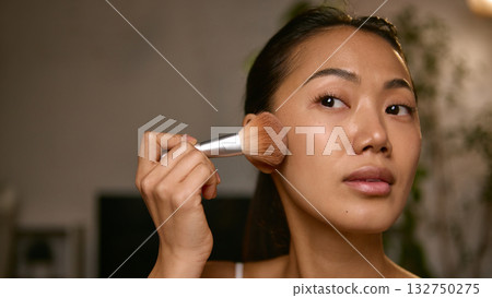 Woman applying blush with brush focusing on natural glow and tone Woman applying blush with brush focusing on natural glow and tone 132750275