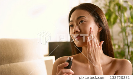 Woman applying serum on cheek with gentle thoughtful touch 132750281