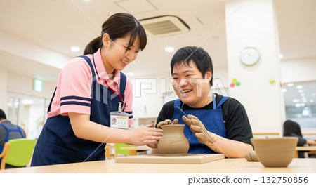 笑容滿面的殘障人士正在享受陶藝創作，一位女性輔助人員在一旁輕柔地協助他們（創意活動）。陶藝課，美術活動 132750856