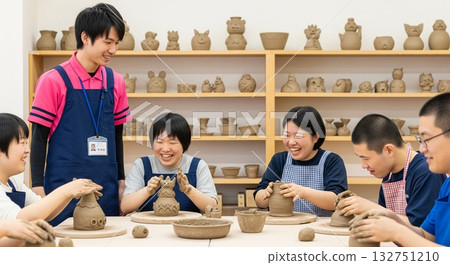 A male support worker (welfare/workshop) interacting with users with a smile while working with clay. Clay/pottery, creative recreation 132751210