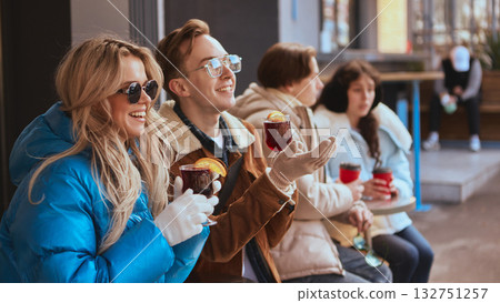 Group of young friends laughing and drinking hot beverages outdoors Group of young friends laughing and drinking hot beverages outdoors 132751257