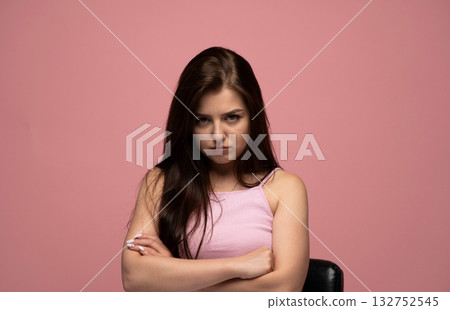 Angry brunette woman with long hair crossing arms and frowning on pink background 132752545