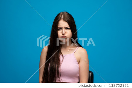 Brunette woman with long hair puffing cheeks and making funny face on blue background 132752551