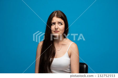 Confused brunette woman with long hair looking aside on blue studio background 132752553