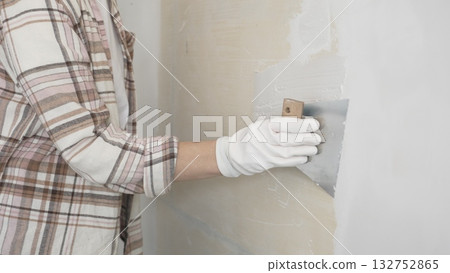 Unknown female construction worker wearing protective gloves applying plaster, smoothing wall surface during home renovation work 132752865