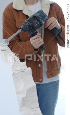 Unrecognizable construction worker demolishing concrete wall with rotary hammer, wearing protective safety gear. Renovation concept, closeup vertical view 132752885