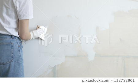 Unknown female construction worker applying plaster with putty knife, smoothing wall surface during home renovation, fixing wall imperfections with professional drywall repair technique, close up Unknown female construction worker applying plaster with putty knife, smoothing wall surface during home renovation, fixing wall imperfections with professional drywall repair technique, close up 132752901