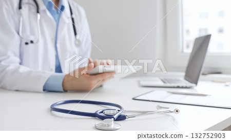Closeup of blue stethoscope is lying on the table near female doctor reviewing prescription on digital tablet, representing digital healthcare workflow in contemporary medical setting. Medicine Closeup of blue stethoscope is lying on the table near female doctor reviewing prescription on digital tablet, representing digital healthcare workflow in contemporary medical setting. Medicine 132752903