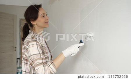 Woman wearing protective gloves painting white wall with small paint roller, updating interior and giving room clean, modern look during home renovation project Woman wearing protective gloves painting white wall with small paint roller, updating interior and giving room clean, modern look during home renovation project 132752936