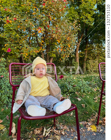 Baby in Yellow Sweater Sits on Red Chair in Autumn Park 132753110