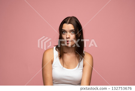 Funny young woman in white tank top making fish face on pink background Funny young woman in white tank top making fish face on pink background 132753676