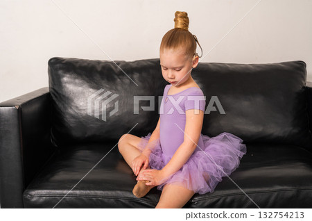 Ballet girl with cochlear implant sitting on sofa touching leg. Hearing rehabilitation, focus, and confidence in inclusive artistic childhood. 132754213