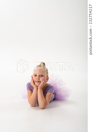 Little ballerina with cochlear implant lying on floor and smiling. Childhood inclusion, relaxation, and hearing awareness through art, grace, and joy. 132754217