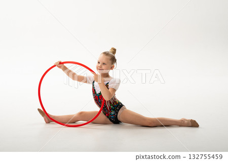 Girl gymnast with cochlear implant performing split with red hoop. Combination of hearing technology, discipline, and inclusion in rhythmic gymnastics and childhood art. 132755459