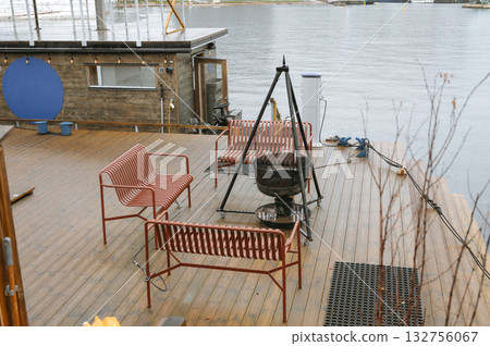 Cozy lakeside patio with red benches and fire pit on wooden deck Cozy lakeside patio with red benches and fire pit on wooden deck 132756067