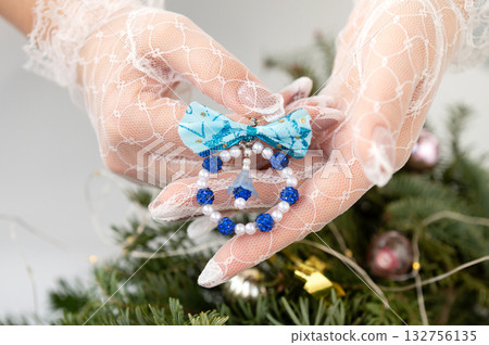 Delicate lace-gloved hands holding blue christmas ornament near tree Delicate lace-gloved hands holding blue christmas ornament near tree 132756135
