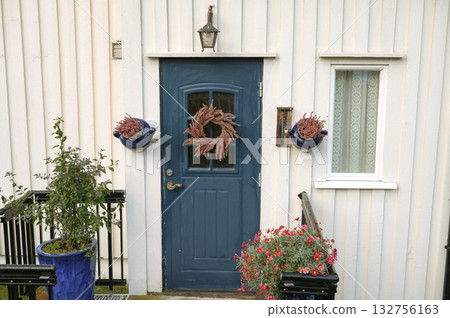 Charming blue door with flowers and wreath on white wooden house exterior 132756163