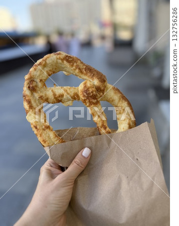 Pretzel in a brown paper bag held outdoors with blurred cityscape in background 132756286