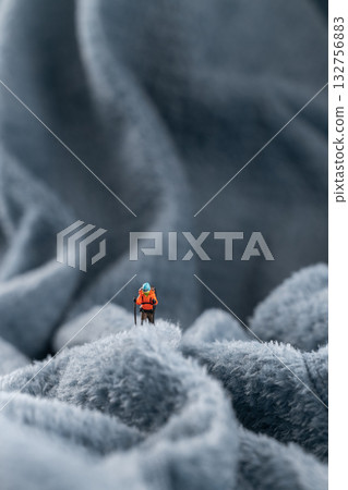 A figurine of a miniature mountain climber, set on a soft fleece surface that mimics a snow-covered landscape, with a hazy backdrop of a mountain or an icy wall A figurine of a miniature mountain climber, set on a soft fleece surface that mimics a snow-covered landscape, with a hazy backdrop of a mountain or an icy wall 132756883