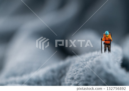 A miniature mountain climber figurine on a fuzzy fleece lining resembling a snow-covered surface, with a blurred background of a mountain or ice wall A miniature mountain climber figurine on a fuzzy fleece lining resembling a snow-covered surface, with a blurred background of a mountain or ice wall 132756892
