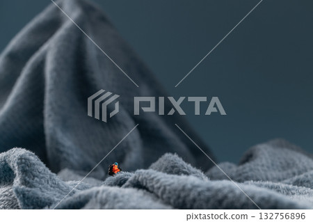A miniature mountain climber figurine on a fuzzy fleece lining resembling a snow-covered surface, with a blurred background of a mountain or ice wall A miniature mountain climber figurine on a fuzzy fleece lining resembling a snow-covered surface, with a blurred background of a mountain or ice wall 132756896