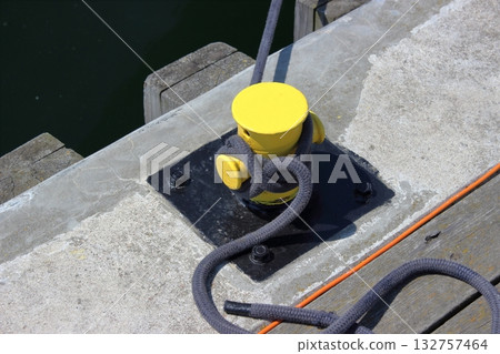 Yellow mooring bollard with rope on pier 132757464
