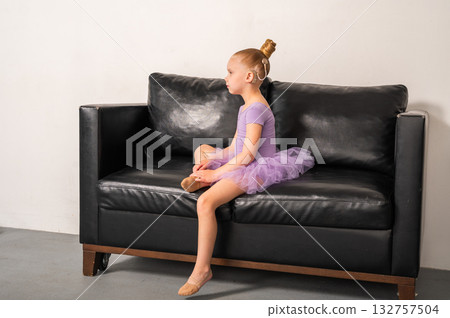 Girl ballerina with cochlear implant sitting on black sofa holding bottle of water. Inclusion, childhood recovery, and empowerment through hearing and rest. Girl ballerina with cochlear implant sitting on black sofa holding bottle of water. Inclusion, childhood recovery, and empowerment through hearing and rest. 132757504