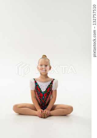 Young girl gymnast with cochlear implant sitting in butterfly pose. Inclusion, recovery, and inclusive spirit of childhood gymnastics and hearing restoration. 132757510