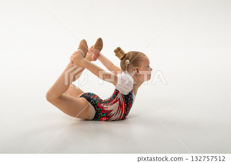 Gymnast child with cochlear implant holding feet in bow pose. Inclusion concept. Harmony of body, sound technology, and resilience in inclusive rhythmic gymnastics. Gymnast child with cochlear implant holding feet in bow pose. Inclusion concept. Harmony of body, sound technology, and resilience in inclusive rhythmic gymnastics. 132757512
