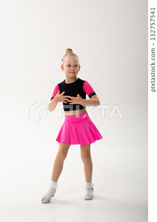 Smiling girl in pink dance outfit with cochlear implant performing studio pose. Celebration of hearing restoration, inclusion, and artistic confidence in children dance and movement. 132757541