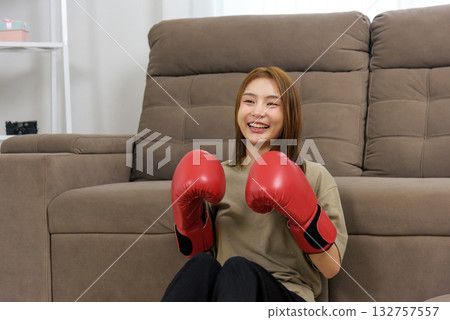 Young happy woman finds joy in home activity, people love such moments, wearing red boxing gloves, beaming wide smile, ready for fitness training, workout goals. Young happy woman finds joy in home activity, people love such moments, wearing red boxing gloves, beaming wide smile, ready for fitness training, workout goals. 132757557