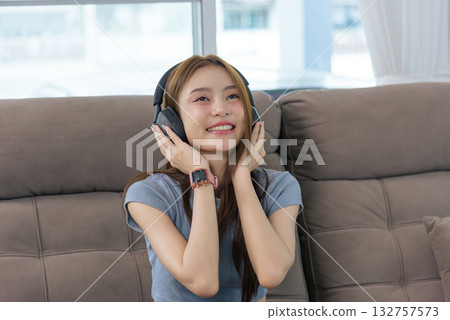 Young woman happy at home, people engaging in relaxing activity, enjoying music through headphones on comfortable sofa, joyful expression, modern lifestyle leisure time indoors. 132757573
