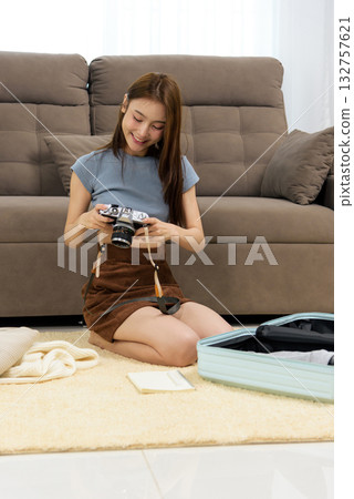 Young happy woman activity at home, preparing travel, smiling while checking vintage camera, packing luggage for exciting journey ahead. Young happy woman activity at home, preparing travel, smiling while checking vintage camera, packing luggage for exciting journey ahead. 132757621
