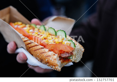 Close-up of street food hot dog with vegetables, corn, and sauce in paper tray outdoors Close-up of street food hot dog with vegetables, corn, and sauce in paper tray outdoors 132757701