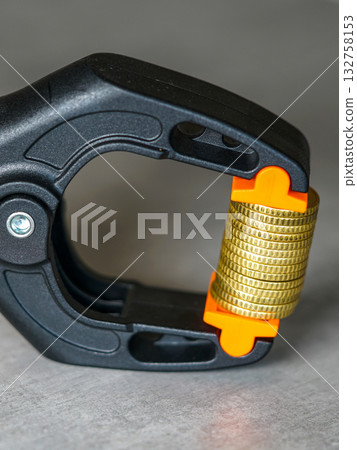 Gold coins squeezed in black and orange clamp symbolizing financial pressure and inflation crisis 132758153